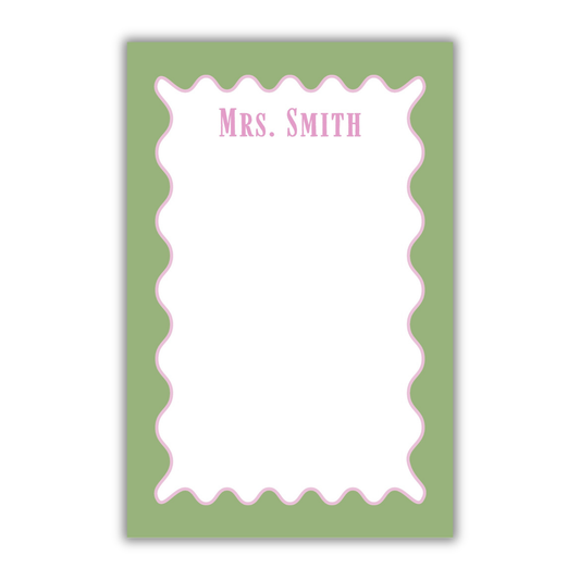 A personalized notepad with a sage green border, a white writing area, a pink scalloped inner border, and the text 'Mrs. SMITH' printed at the top in pink, shown on a white background.