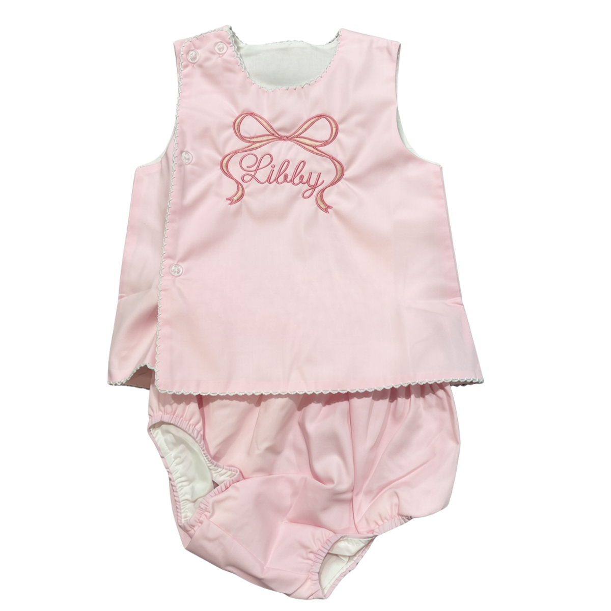 A baby girl's two-piece diaper set consisting of a light pink sleeveless top with trim, buttons and pink embroidered text  under a bow, paired with matching light pink bloomers
