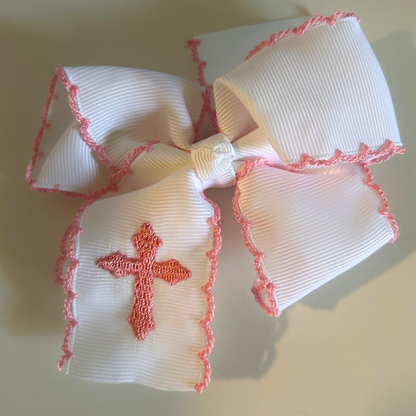A white ribbed grosgrain ribbon hair bow with pink scalloped trim and a pink embroidered cross 