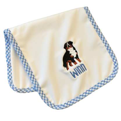 A square cream-colored baby burp cloth with a blue and white gingham border, featuring an embroidered Bernese Mountain Dog and personalized name