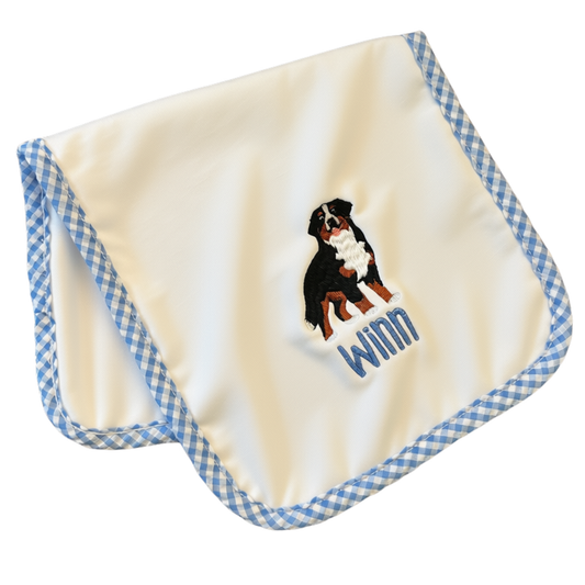 A square cream-colored baby burp cloth with a blue and white gingham border, featuring an embroidered Bernese Mountain Dog and personalized name