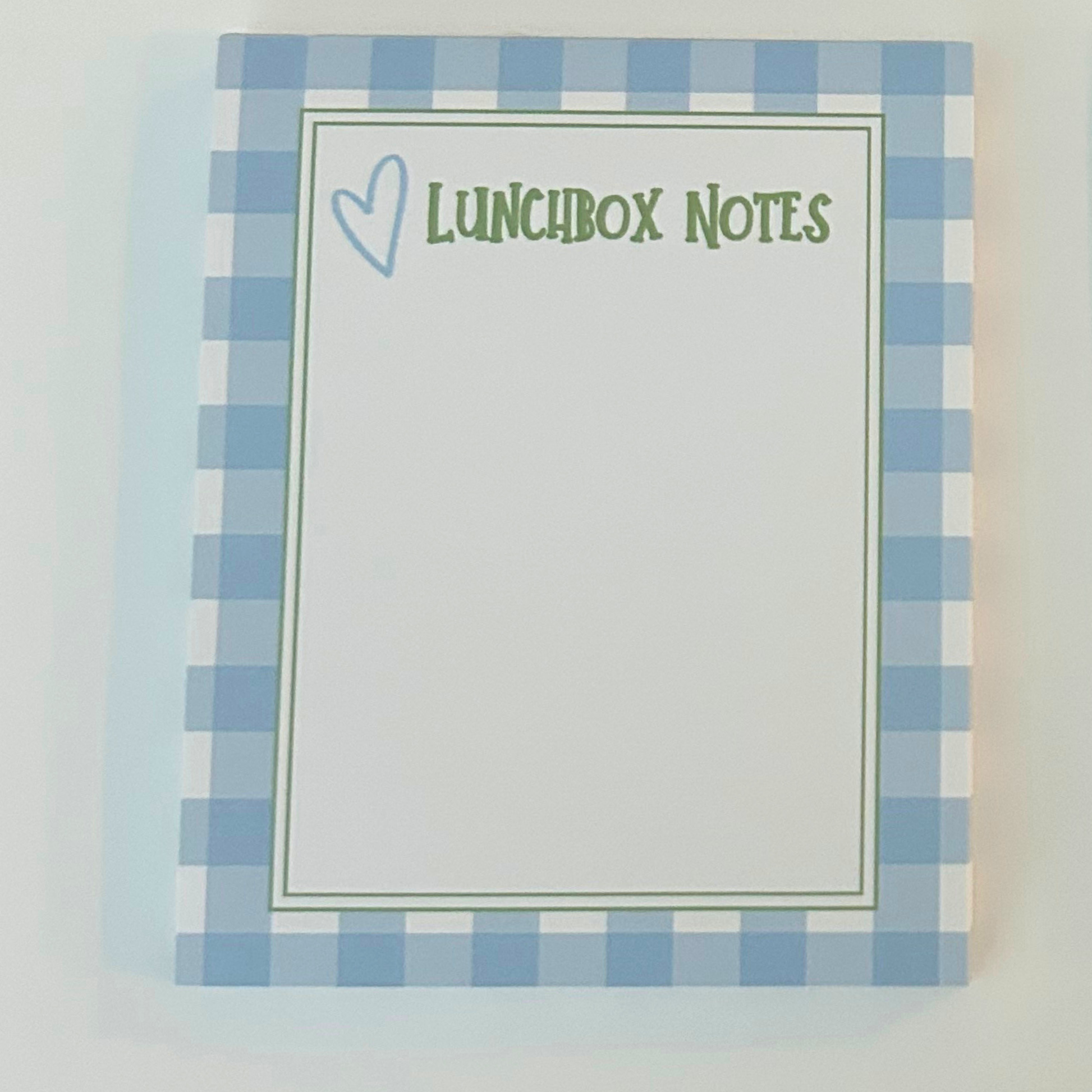 A notepad with a light blue and white gingham border, featuring a white center with the text 'LUNCHBOX NOTES' in green and a small blue heart outline.