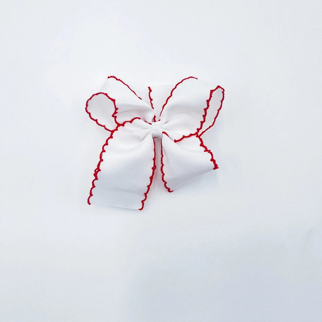 A white fabric hair bow with red scalloped edges,