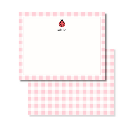 A personalized stationery set featuring a pink and white gingham checkered card. The top card is personalized with a small red ladybug icon and the name printed in black.