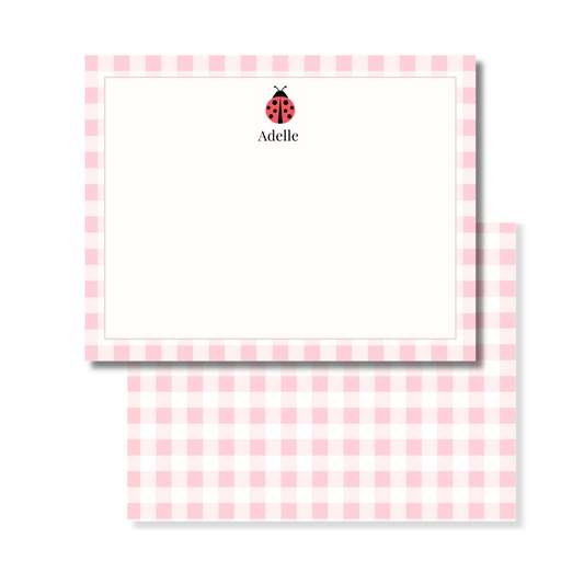 A personalized stationery set featuring a pink and white gingham checkered card. The top card is personalized with a small red ladybug icon and the name printed in black.