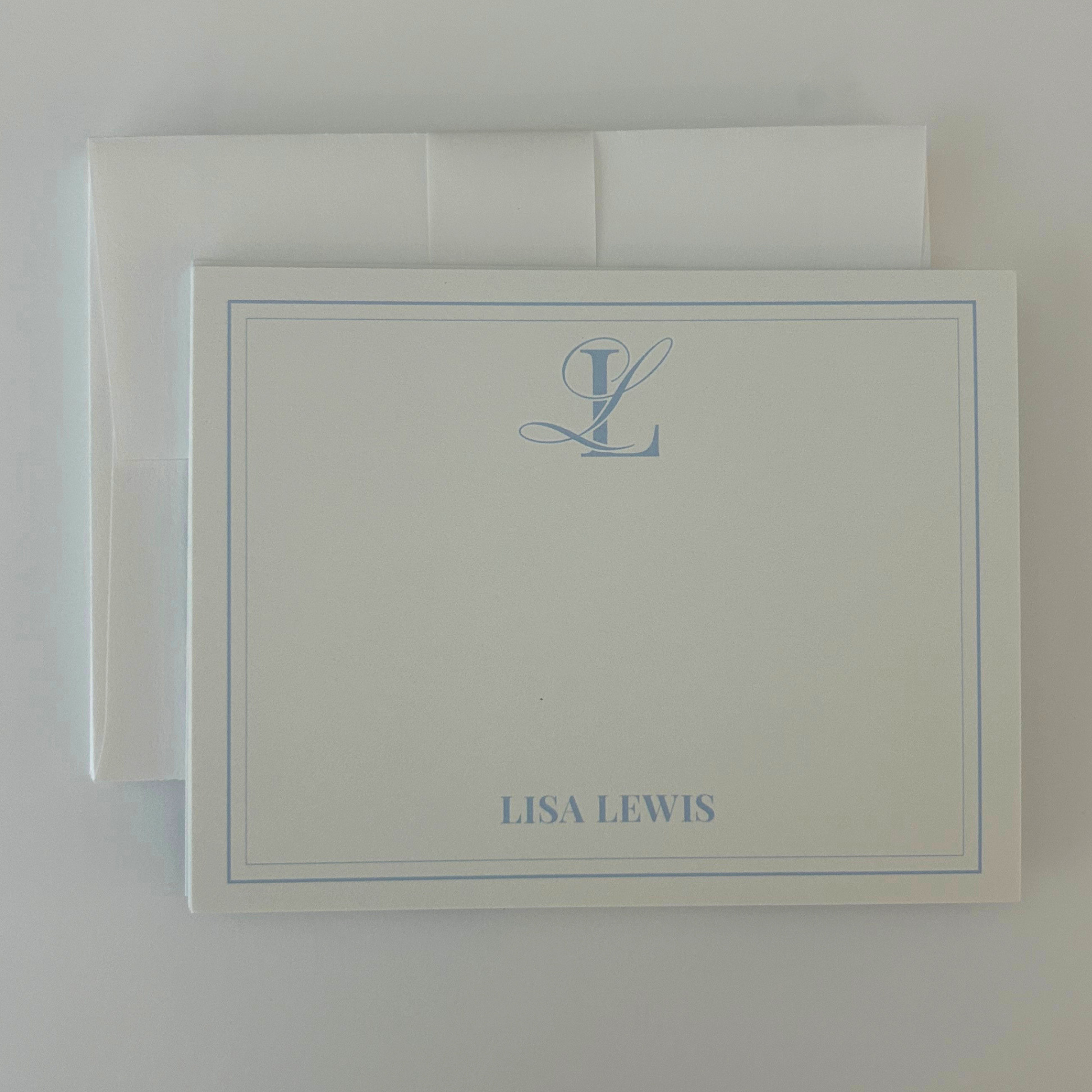 A personalized stationery card with a matching envelope, featuring a light blue monogram and name 