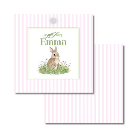A personalized gift tag with a pink and white tripe pattern. The front features a bunny sitting in grass with small pink flowers and custom name.