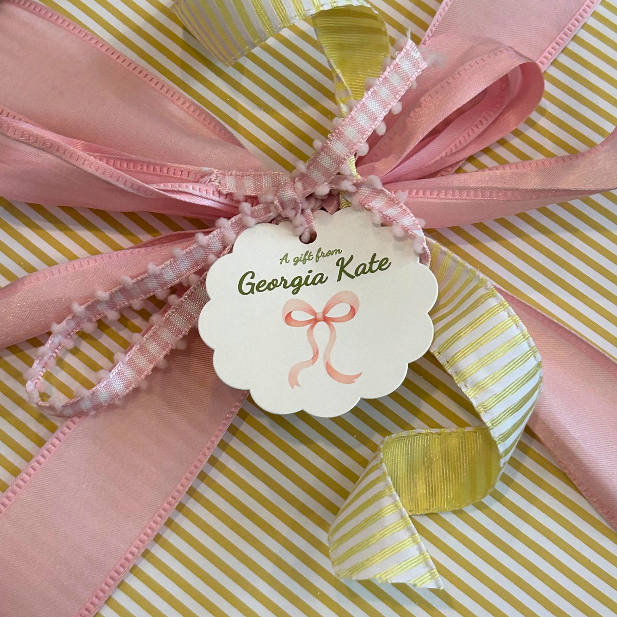 Yellow striped paper, tied with pink and white gingham ribbon, and decorated with a scalloped paper tag personalized