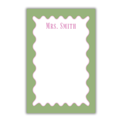 A personalized notepad with a sage green border, a white writing area, a pink scalloped inner border, and the text 'Mrs. SMITH' printed at the top in pink, shown on a white background.