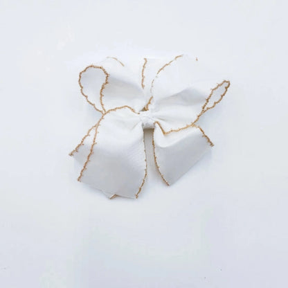 A white fabric hair bow with delicate tan trim