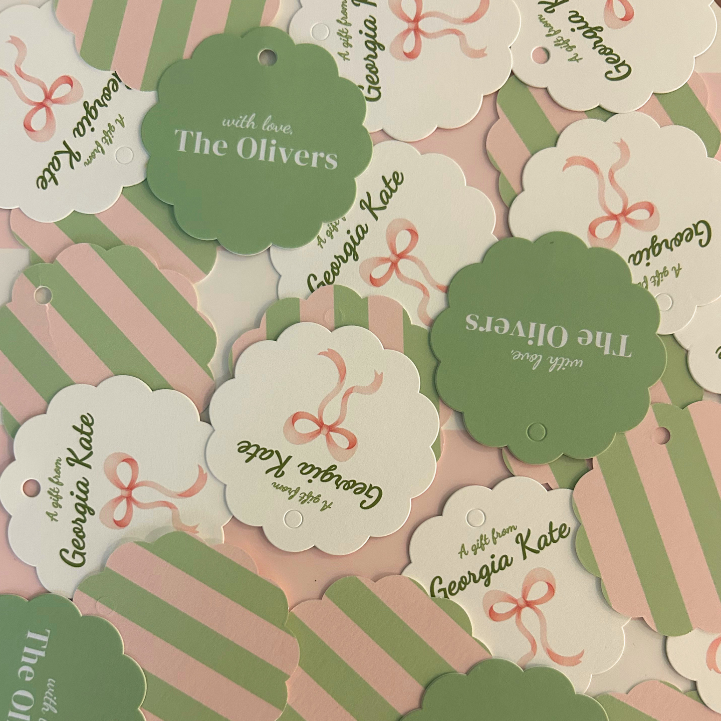 decorative paper tags or labels in pastel pink, sage green, and white, with scalloped and striped shapes, bows, and printed text 