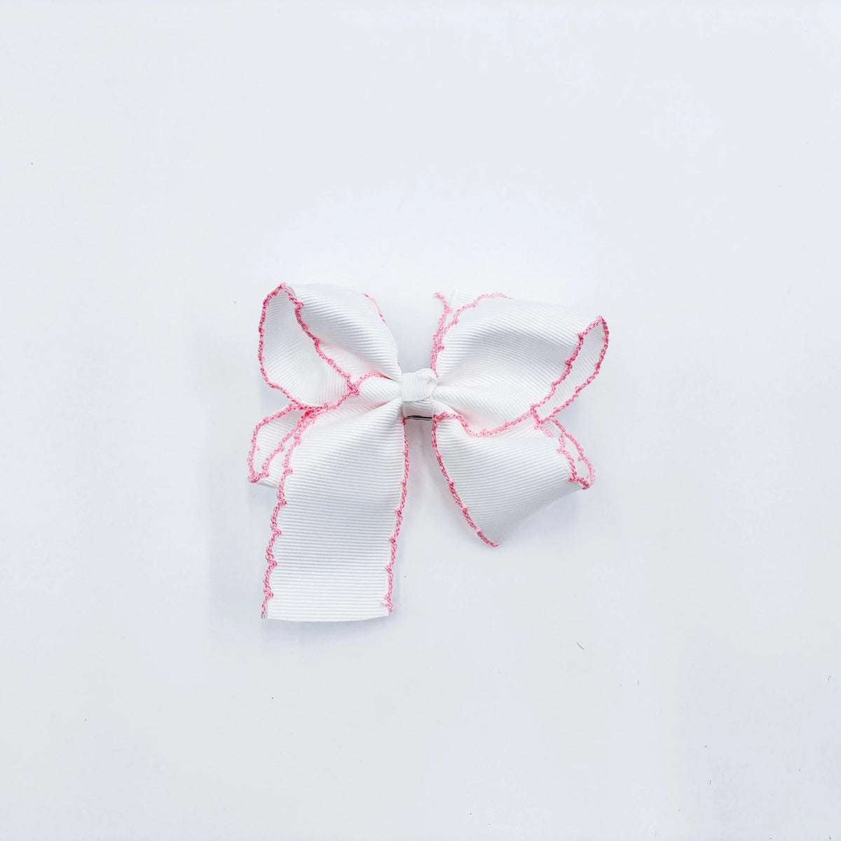 A small white fabric bow with pink zigzag trim