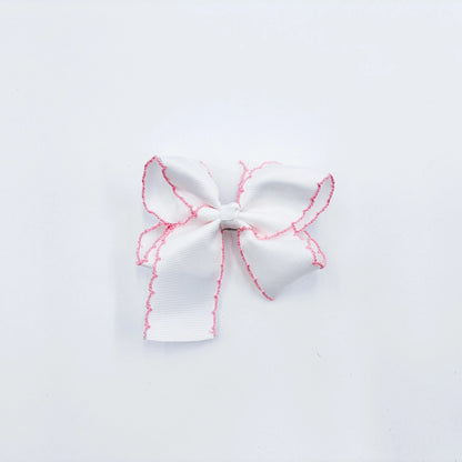 A small white fabric bow with pink zigzag trim